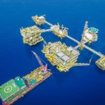 Vista aérea de uma plataforma offshore em alto-mar, com estruturas industriais e equipamentos de produção.