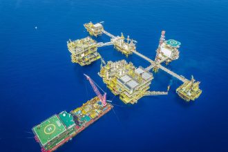 Vista aérea de uma plataforma offshore em alto-mar, com estruturas industriais e equipamentos de produção.