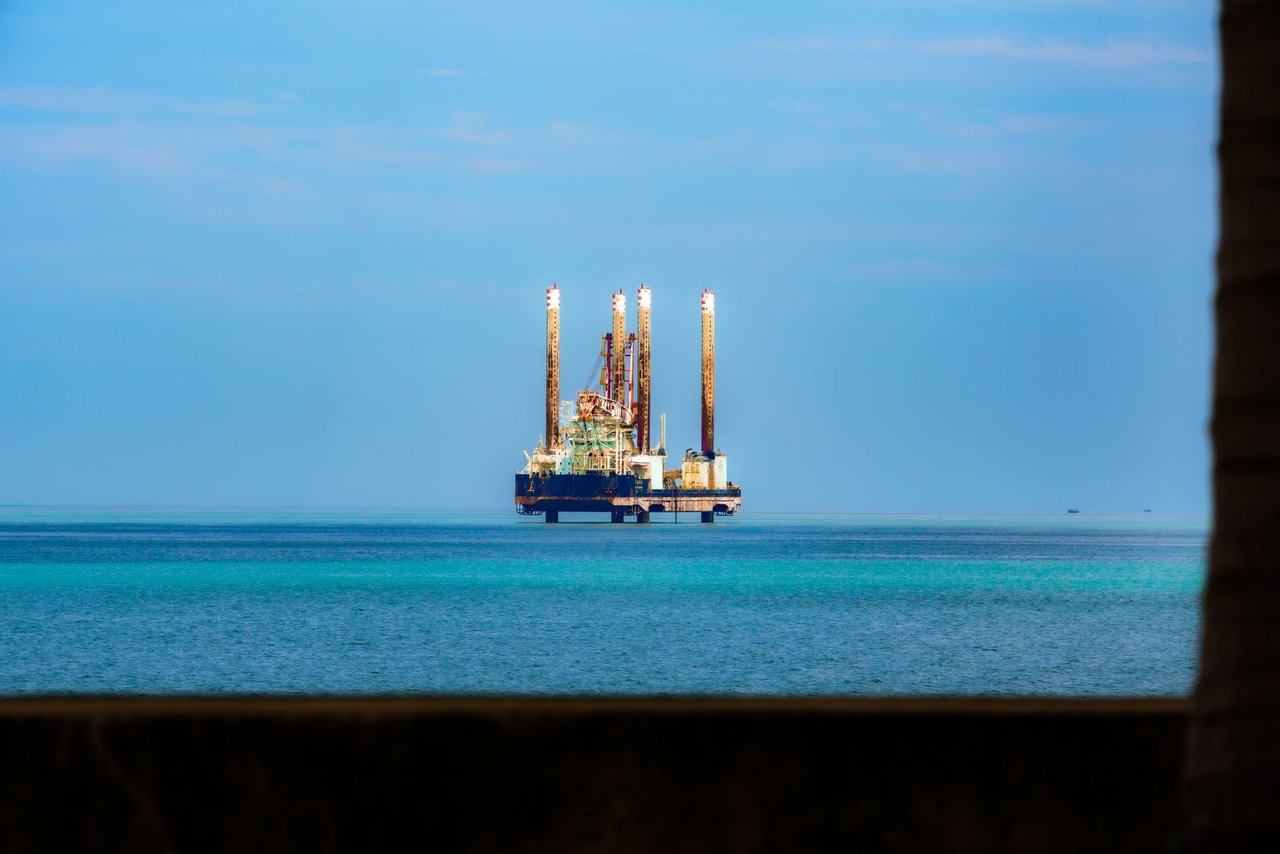 Plataforma de petróleo vista à distância em meio ao oceano, sob céu azul.