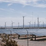 Parque de energia renovável com turbinas eólicas e painéis solares sob céu aberto.