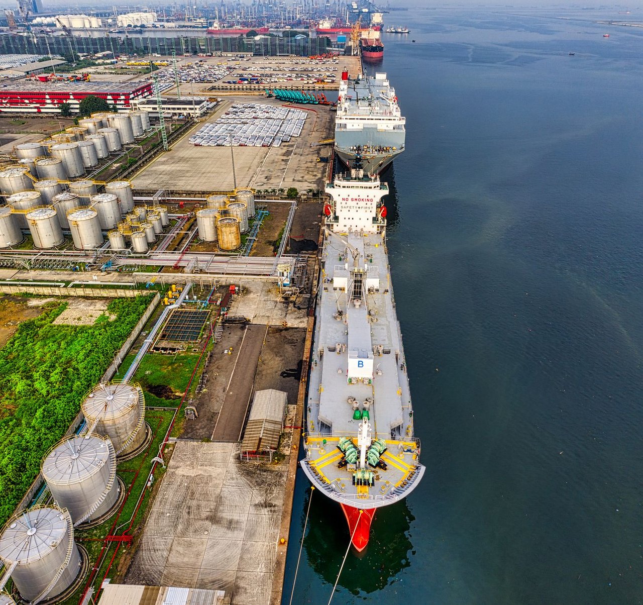Vista aérea de petroleiros junto a instalações industriais de armazenamento de petróleo em um porto.