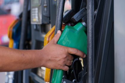 Mão segurando um bico verde de abastecimento em uma bomba de combustível.