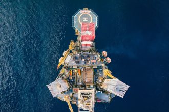 Vista aérea de uma plataforma de petróleo e gás em alto-mar, cercada pelo oceano.