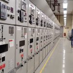 Sala de controle industrial com uma longa fileira de painéis elétricos e instrumentos de monitoramento.