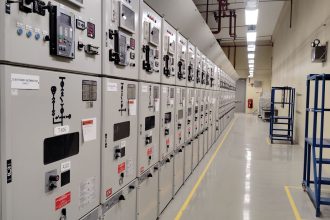 Sala de controle industrial com uma longa fileira de painéis elétricos e instrumentos de monitoramento.